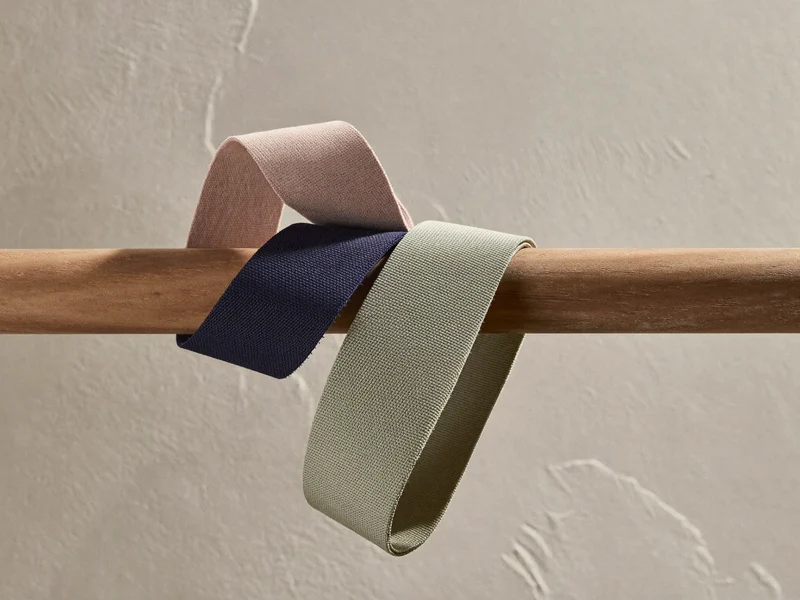 Textil-Widerstandsbänder in mehreren Farben über einer Holzstange vor verputzter Wand